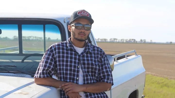 Donate to help Mwenda, Mwenda is leaning on a truck on a farm.